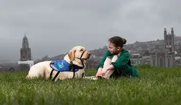 Assistance Dog Keano sitting on grass with a young girl in a traditional irish dance costume