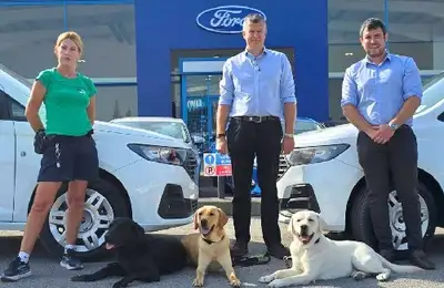 IGD trainer with 3 Ford staff members standing in a Ford forecourt with 3 dogs lying on the ground