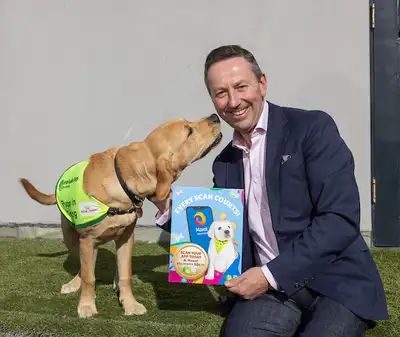 Maxol CEO holding a sign with details of the Every Scan Counts intiative. There is a pup sniffing Brian's face.