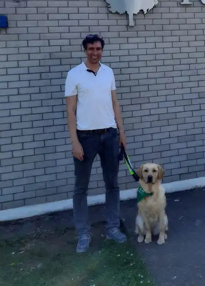 Pippin sitting beside his handler who is standing beside him