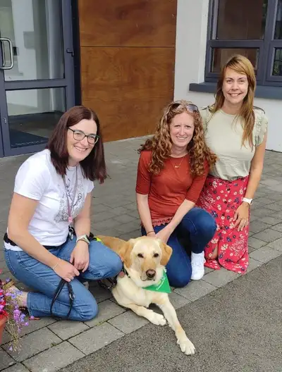 Three teachers kneeling down with Ernesto lying between them