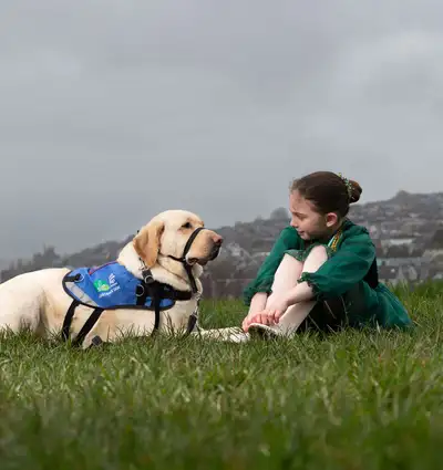 Assistance Dog Keano sitting on grass with a young girl in a traditional irish dance costume